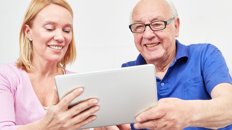 Frau und älterer Mann schauen auf Tablet